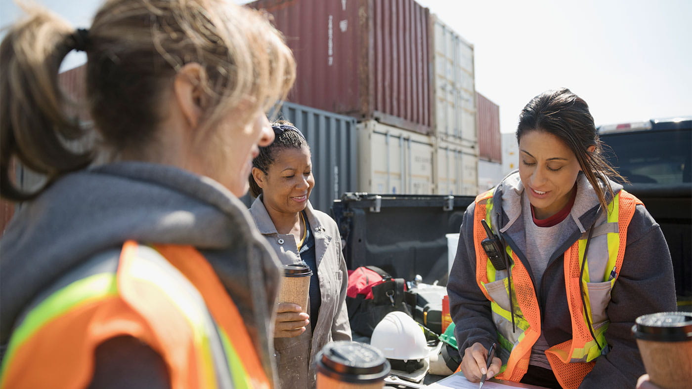 Three women on a construction site in hi visibility vests looking at some paperwork.